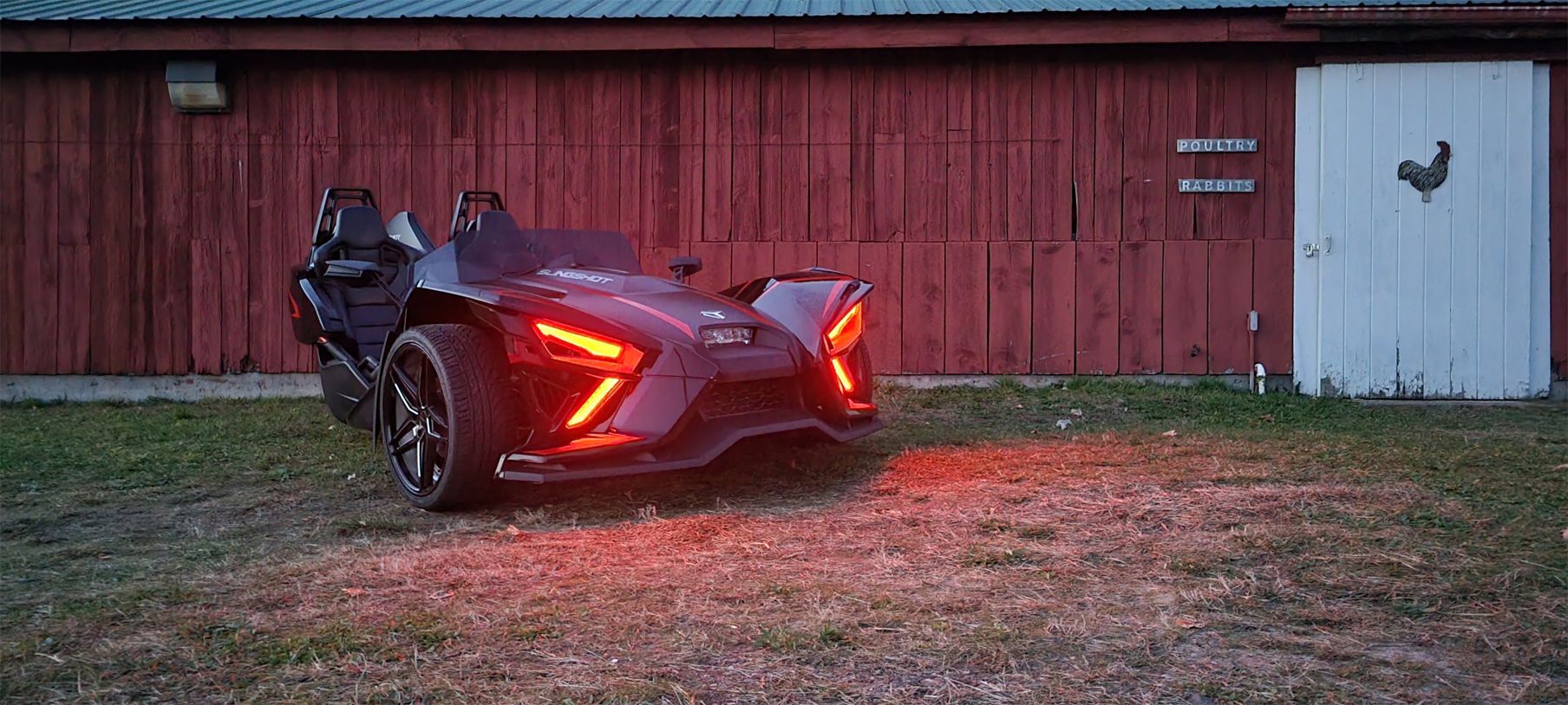 A slingshot is parked in front of a red barn.