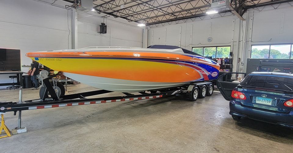 A boat is on a trailer in a garage next to a car.