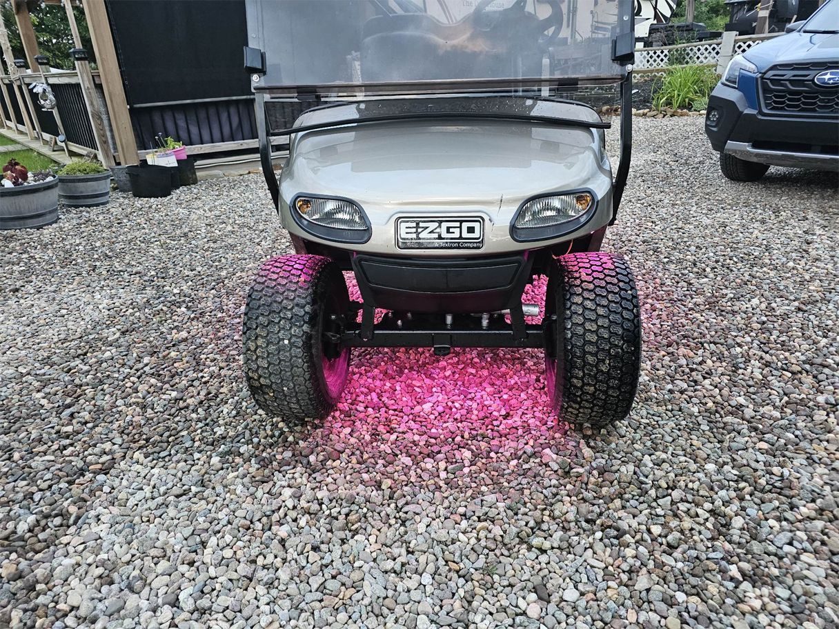 A golf cart is parked on a gravel driveway next to a car.