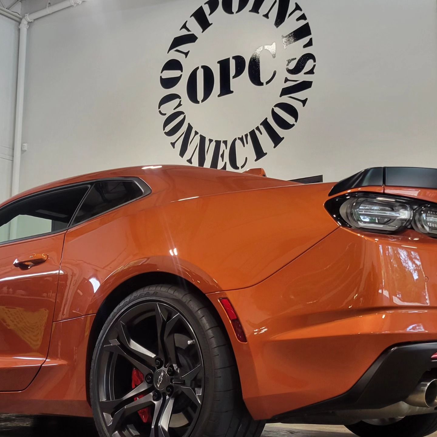 An orange car is parked in front of a sign that says opc connections