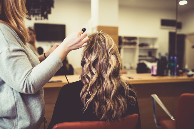 Stylist curling a client's blonde hair in a salon chair