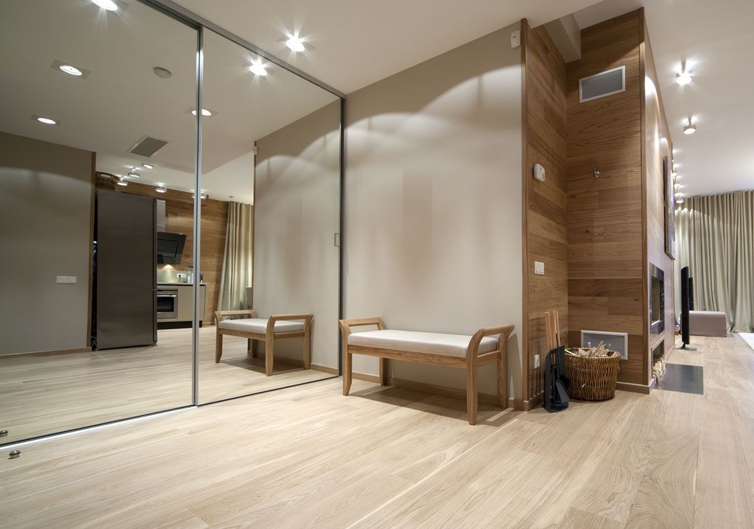 Modern interior with a full-length mirror, wooden bench, light wood flooring, and a wood-paneled wall.