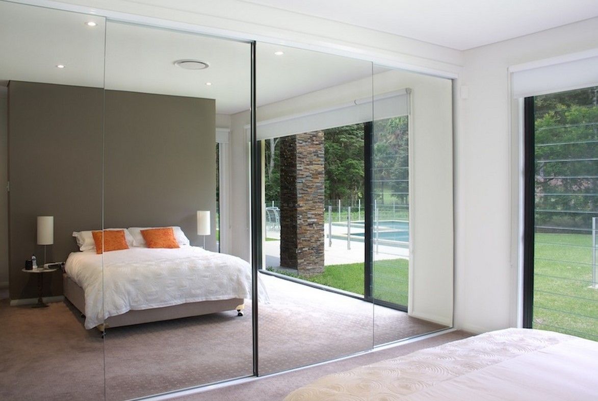 Bedroom with mirrored closet doors reflecting the bed, windows, and a green yard.