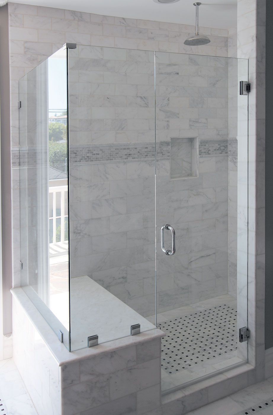 Glass shower enclosure with marble walls and built-in bench.