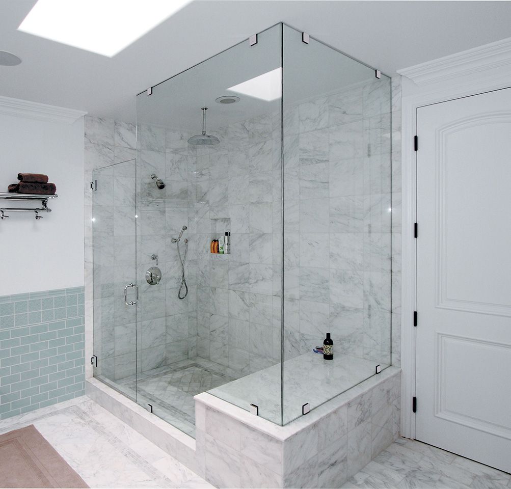 Spacious marble shower with glass walls and a bench; a white door is visible on the right.
