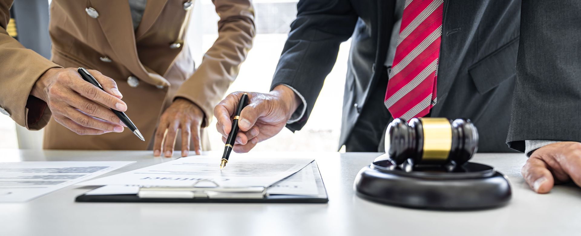Three people review paperwork with pens, a gavel sits on a table.