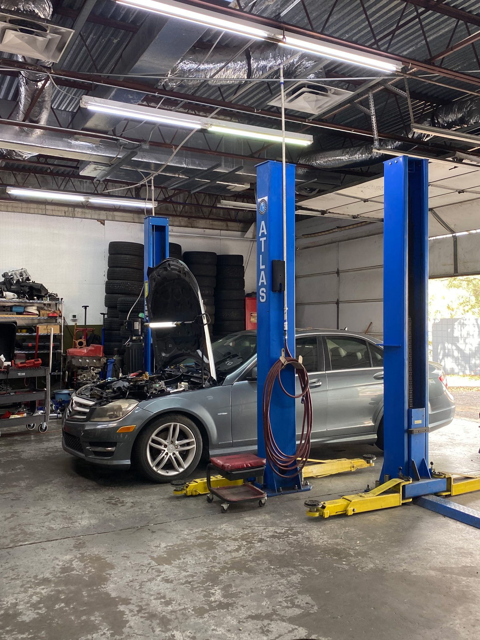 Car raised on a blue lift in a repair shop. Open hood, tires in background.