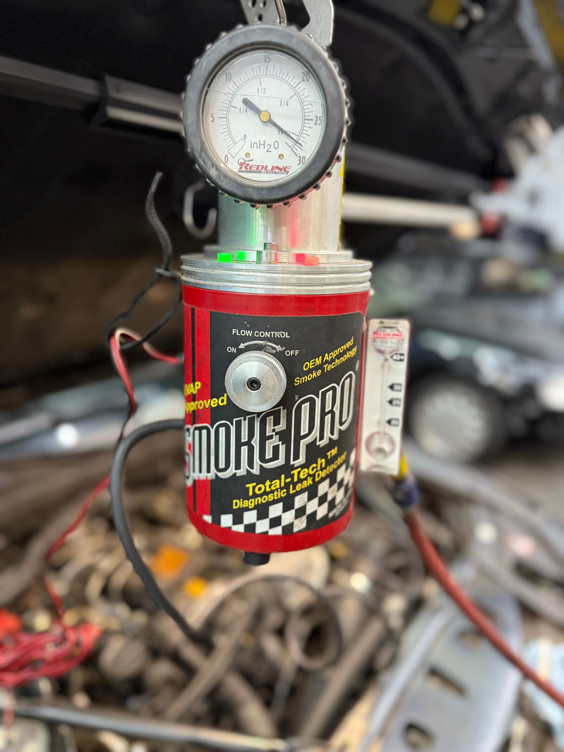 Smoke Pro machine connected to a car engine, used to detect leaks. Gauge and red canister visible.