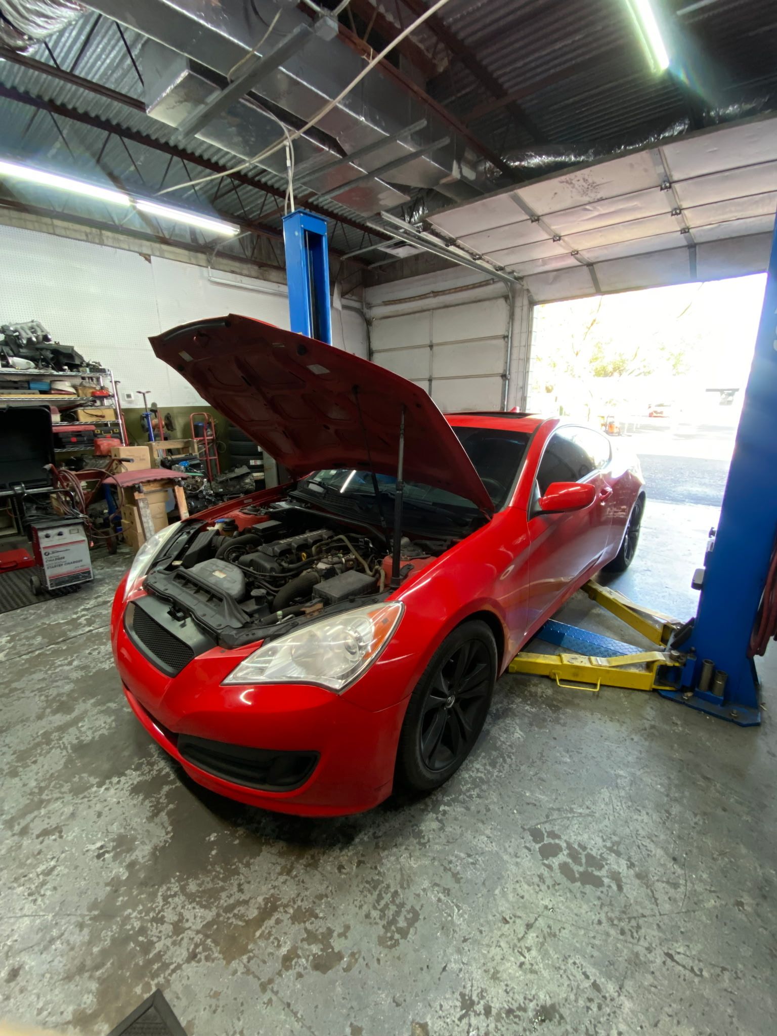 Red car with hood open, on a lift in a garage.