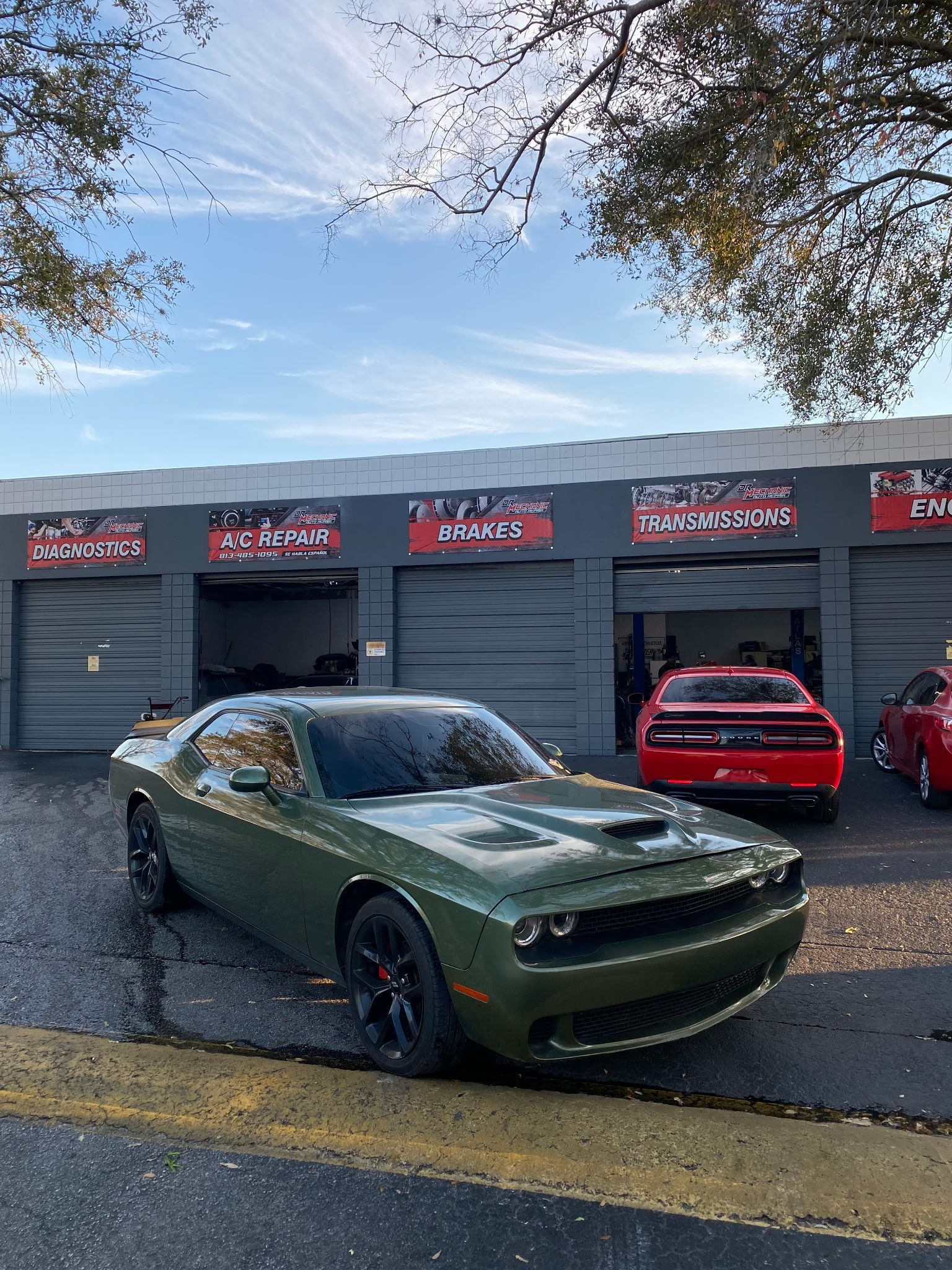 Green Dodge Challenger parked in front of a garage, with red Challengers visible inside.