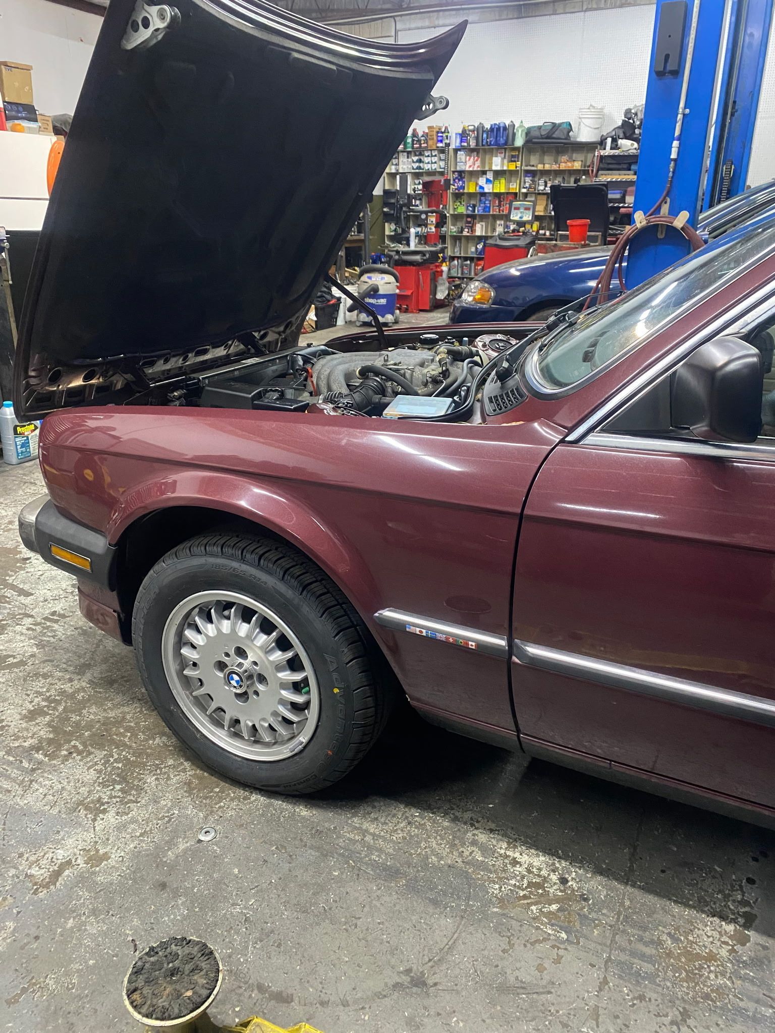 Red BMW sedan with hood open in a garage, revealing engine components; silver rims.