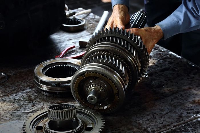 Mechanic's hands holding gears. Gear parts are laid out on a dark, oily workbench.