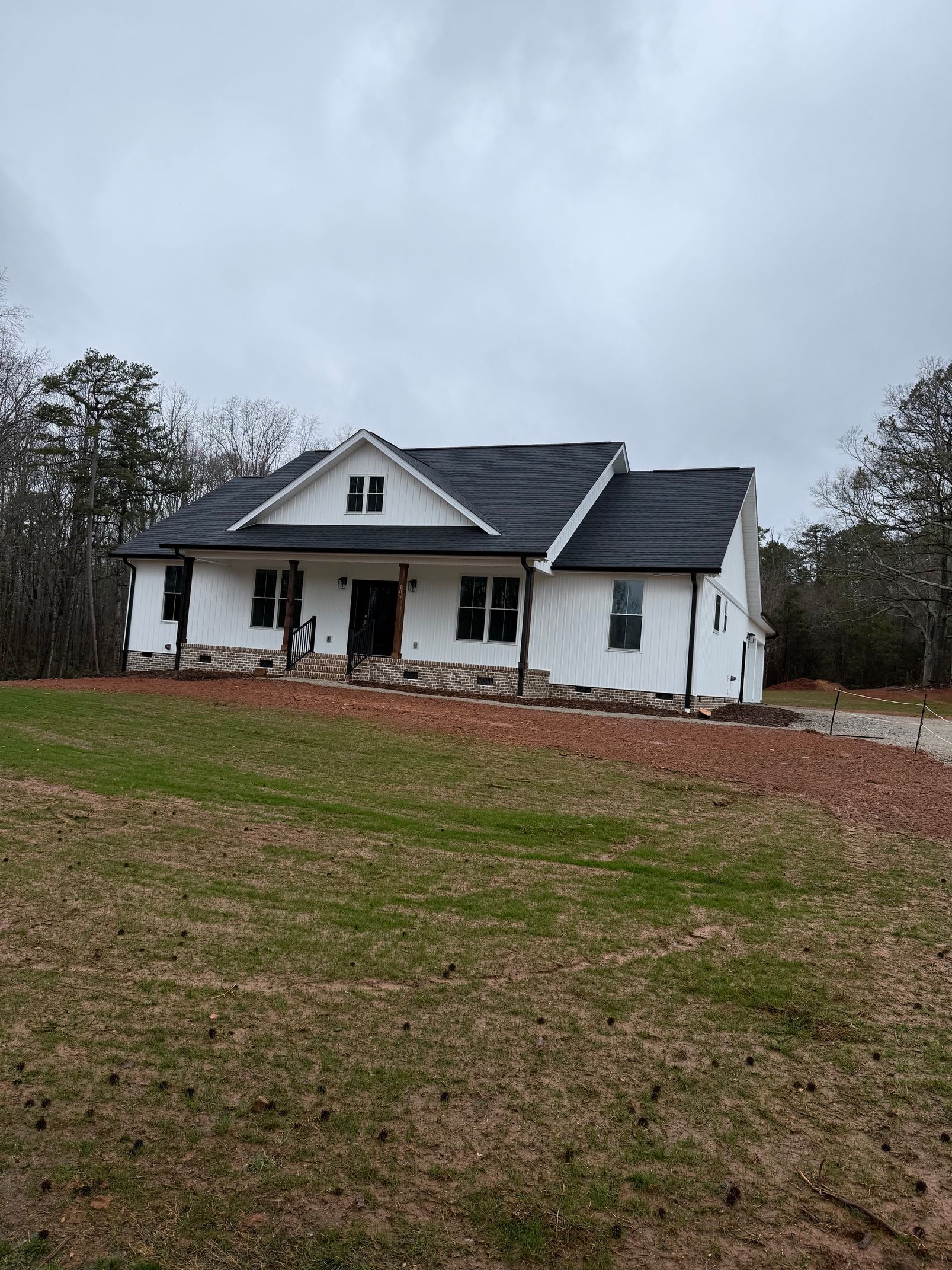 White farmhouse with a dark roof on a grassy lot under an overcast sky