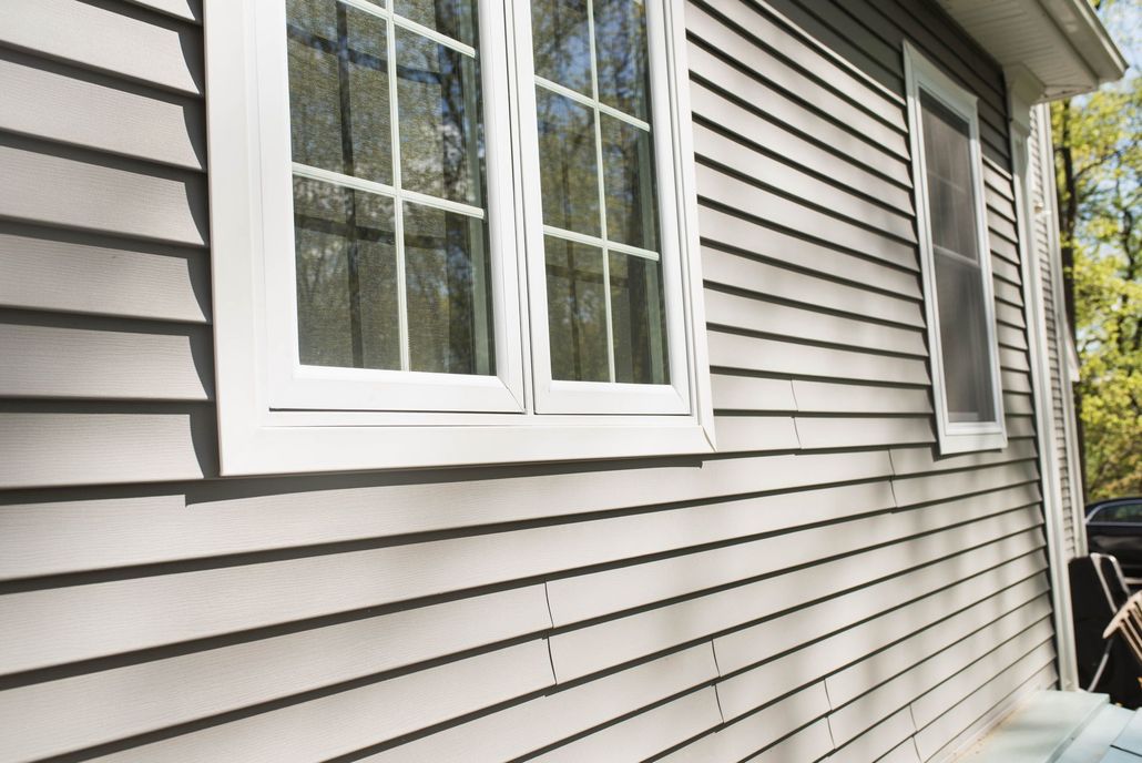 Beige rain gutter on a house corner against a cloudy blue sky.