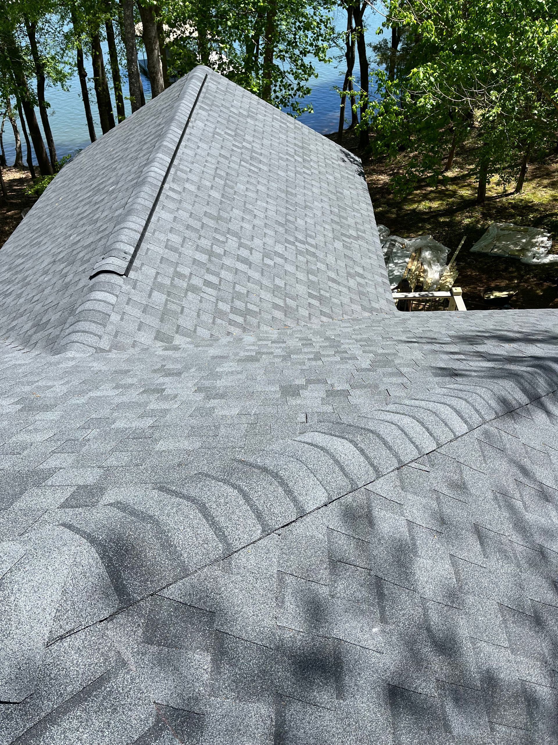 Gray shingled roof peak with trees and dappled sunlight in the background