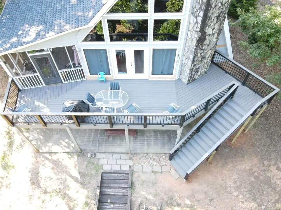 A-frame house with a gray deck, stairs, and stone walkway. Black railing surrounds the deck.