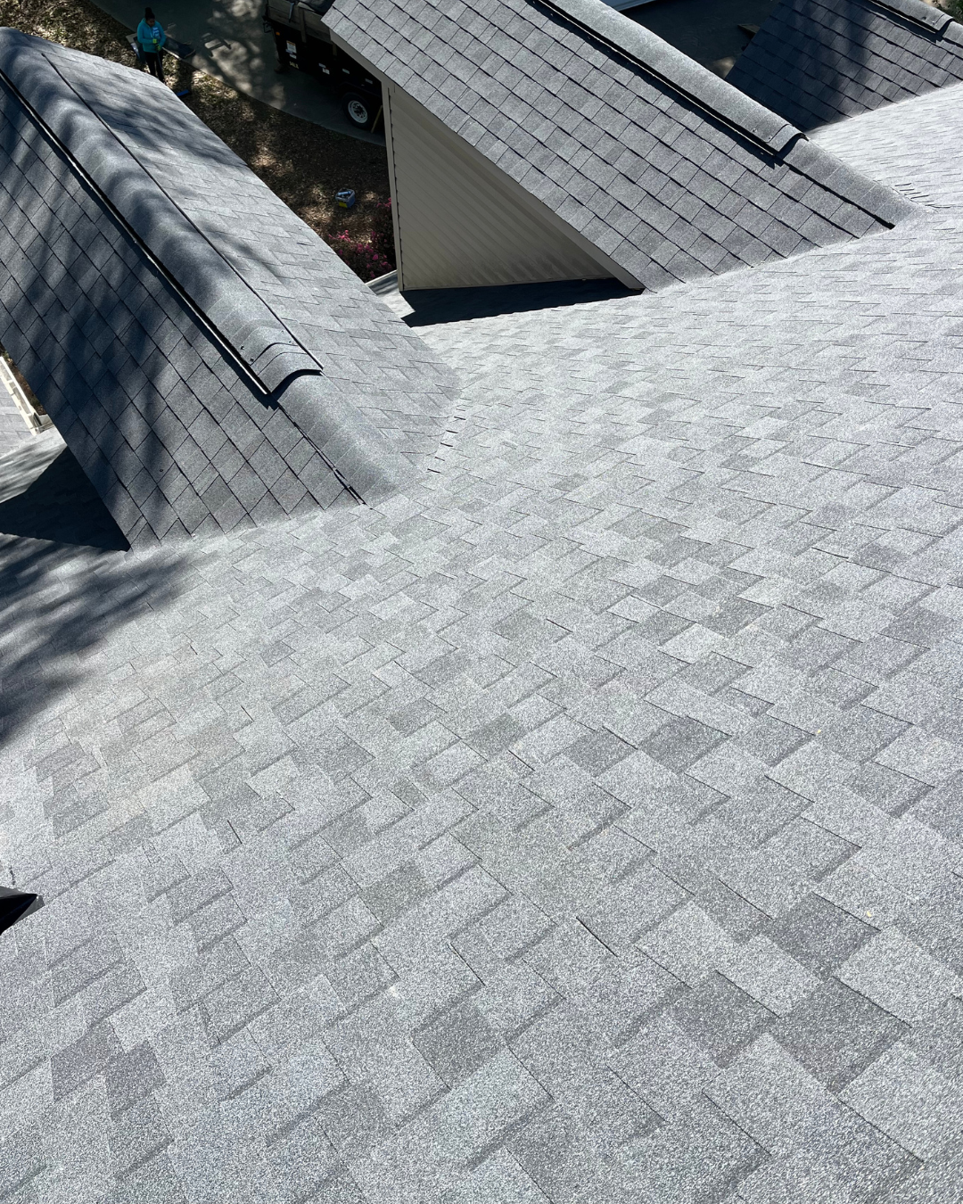 Gray shingle roof with a dormer and chimney in bright daylight