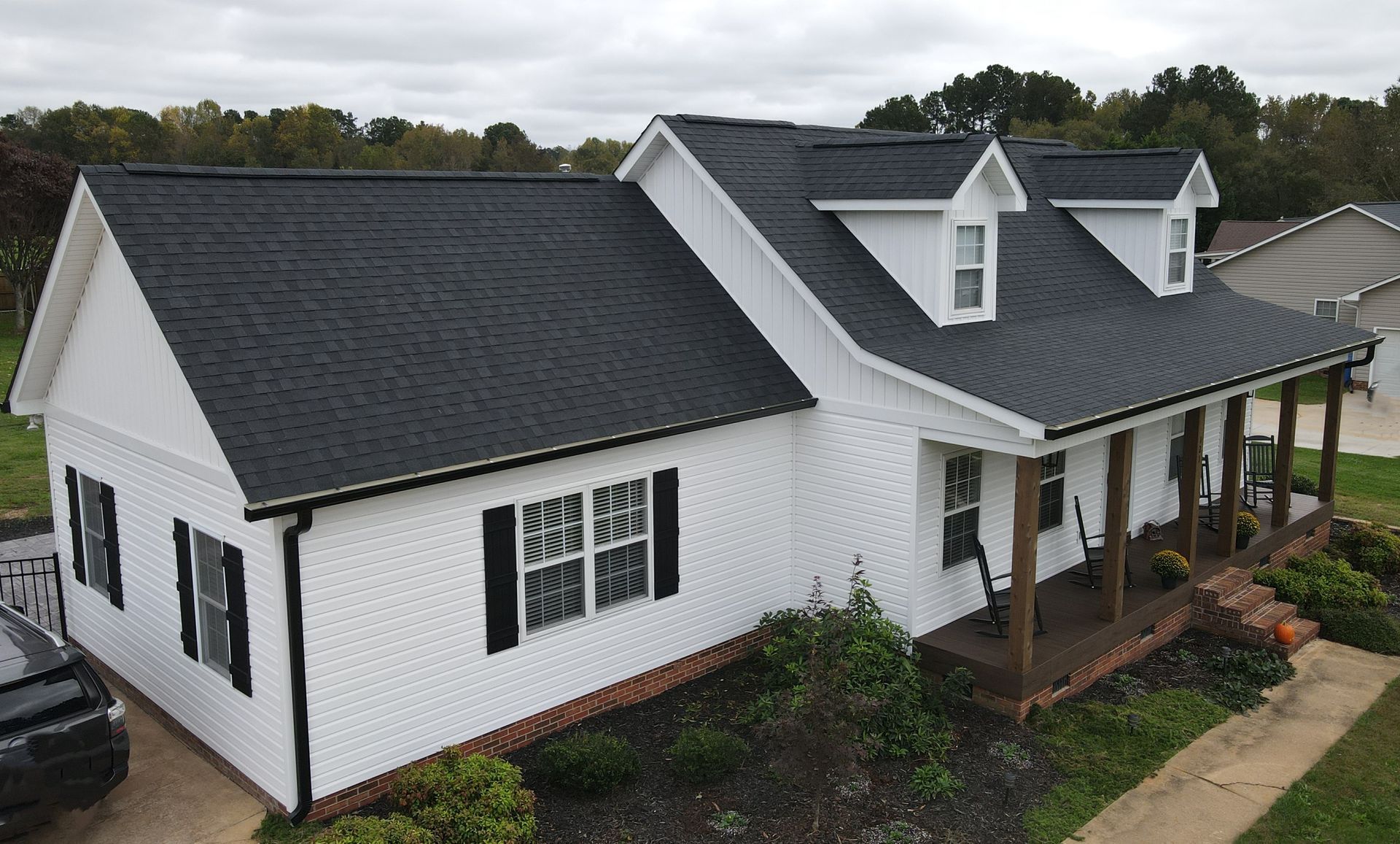 White farmhouse with dark roof and porch, seen from above in a landscaped yard