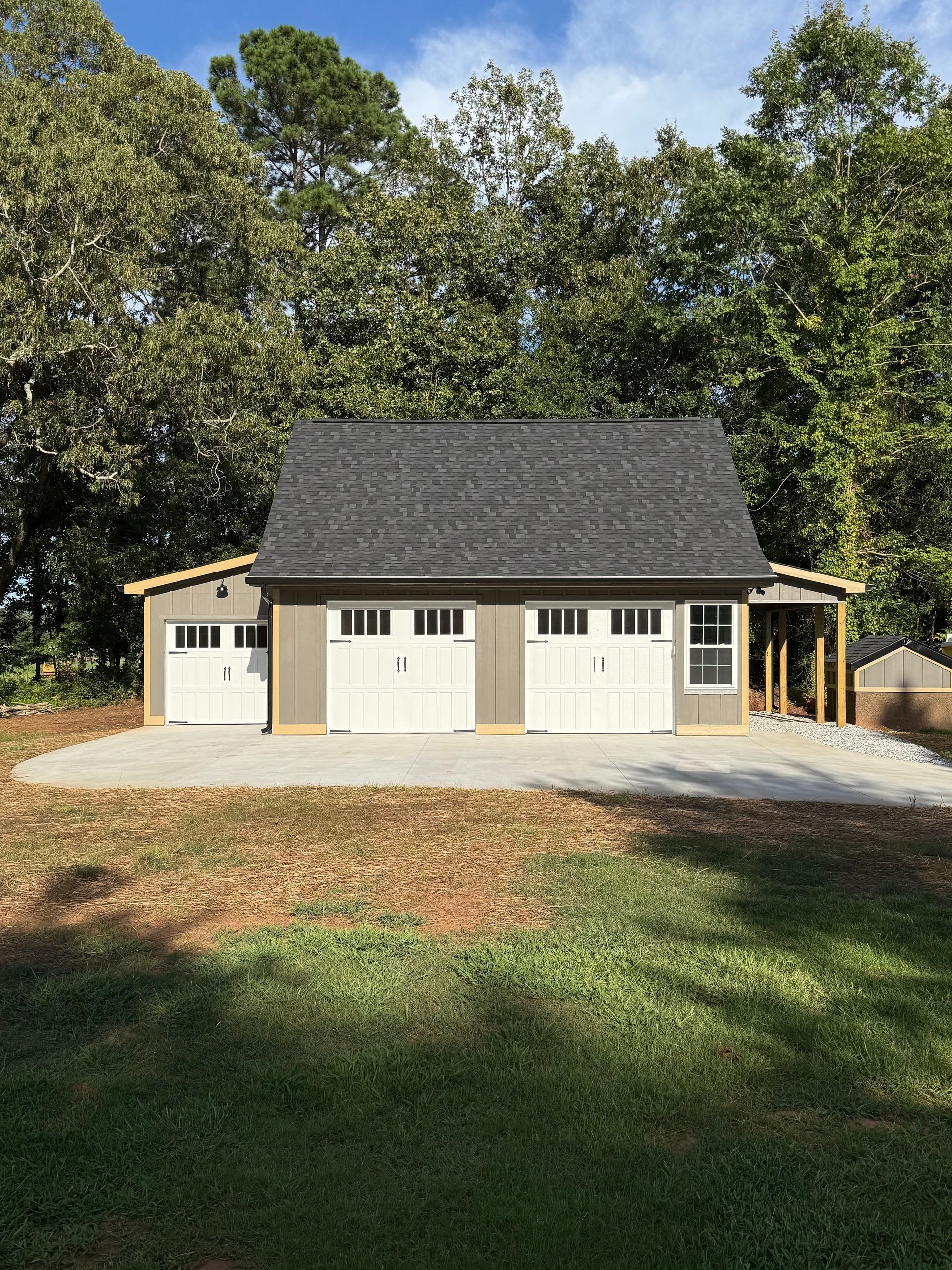 Gray and white two-car garage with black roof, set on a concrete pad, surrounded by trees.