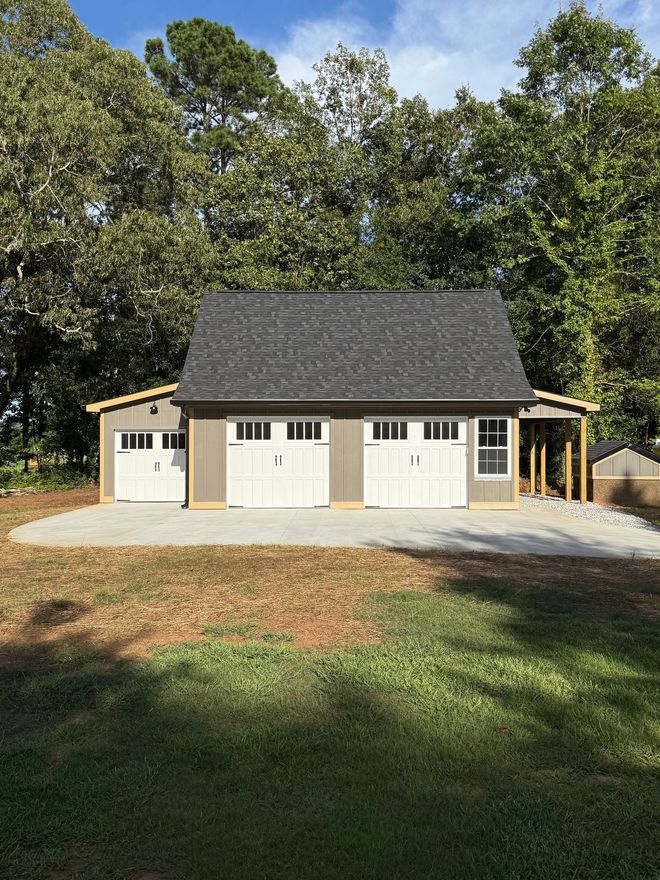 Gray and white two-car garage with black roof, set on a concrete pad, surrounded by trees.