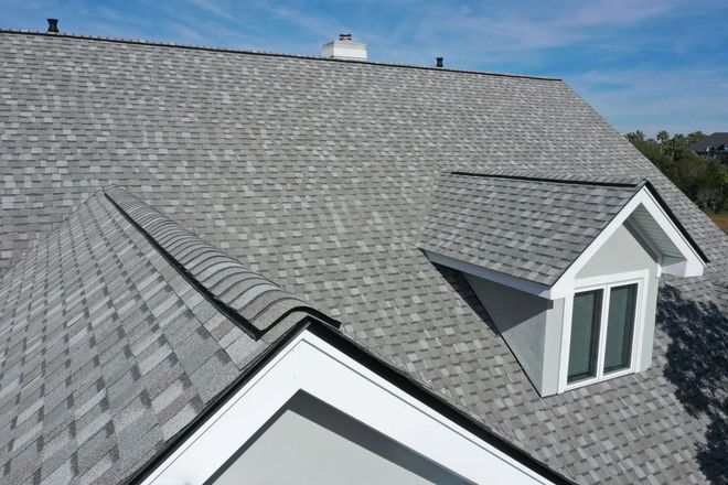 Grey shingle roof on a house with a dormer and chimney against a blue sky.