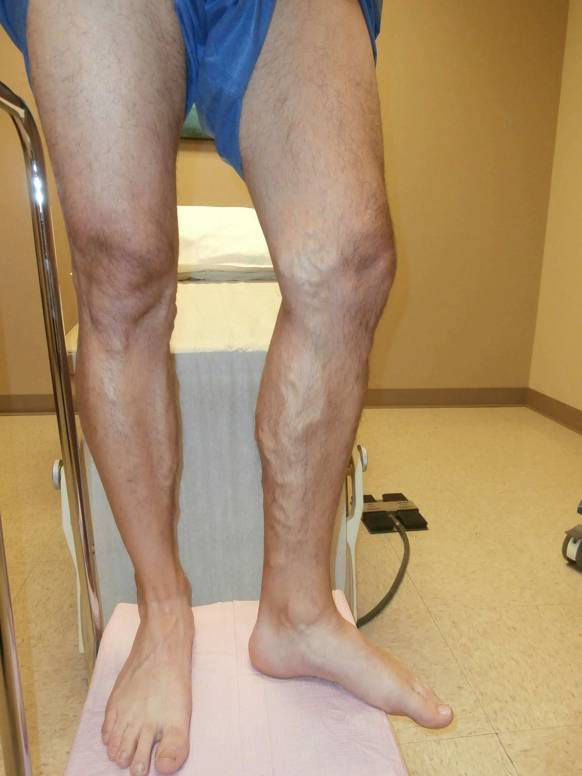 Person standing on a pink platform, right leg bent, left leg straight, with support bar in a medical setting.