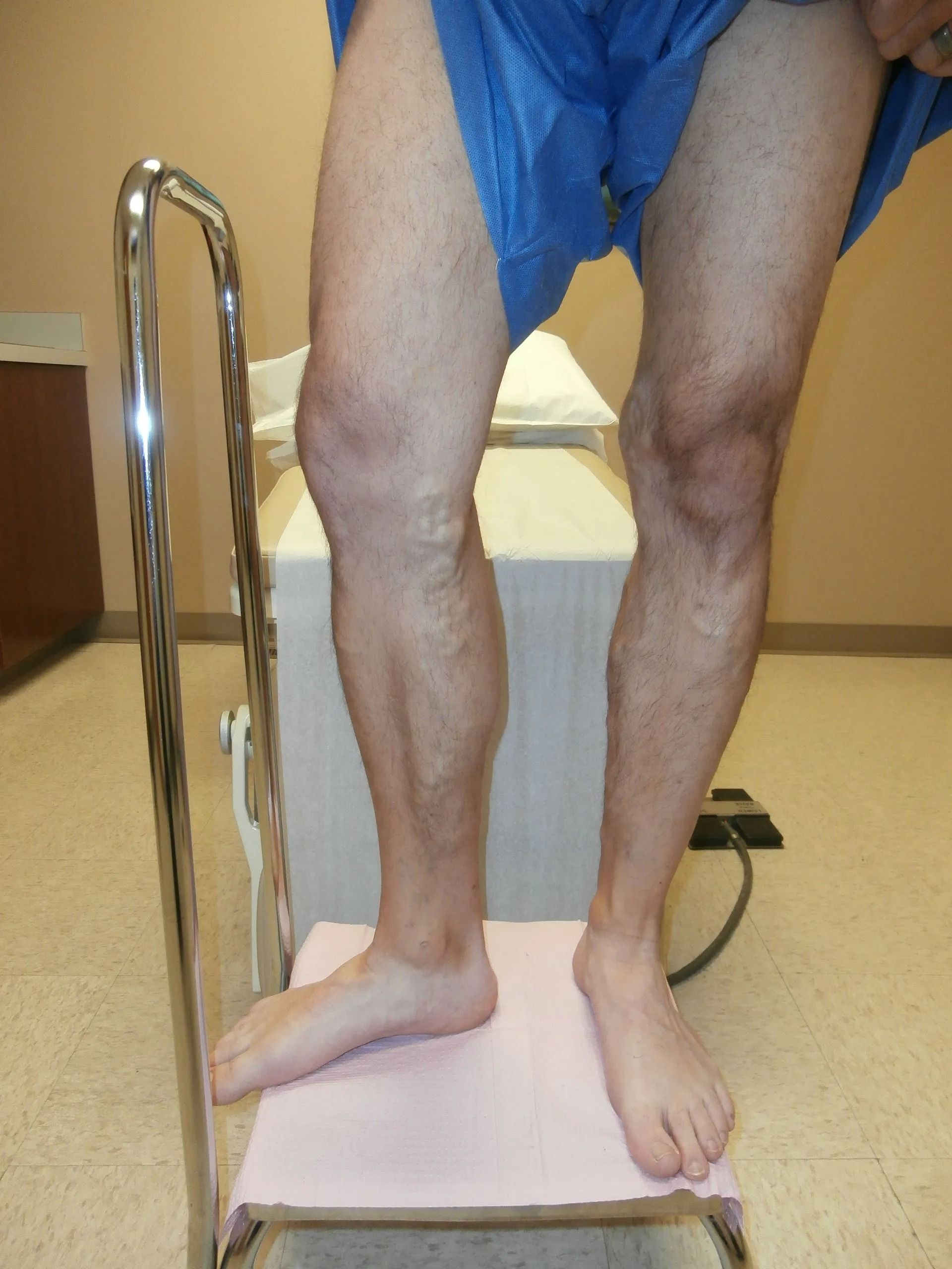 Person standing on a step, supporting themselves with a bar, leg bent, possibly for exercise or therapy.