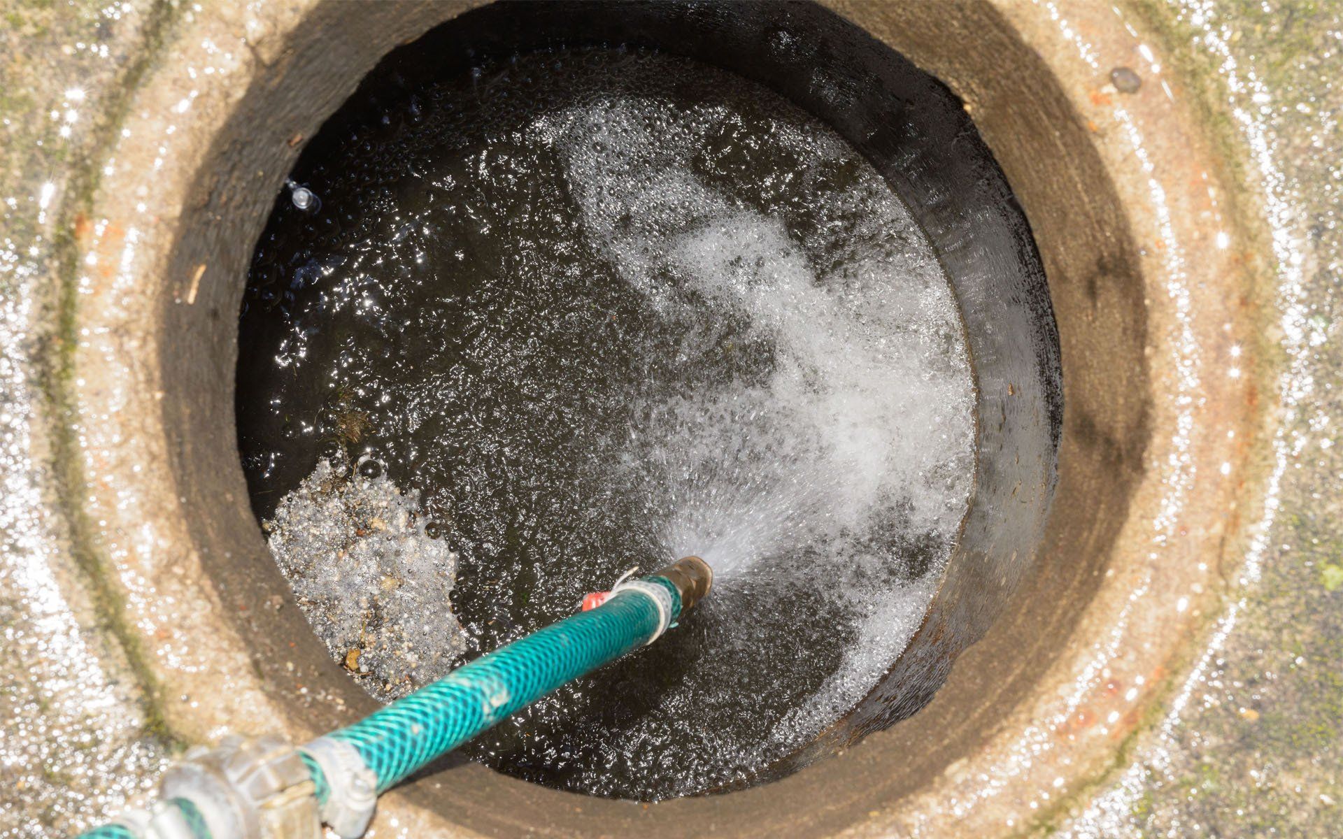 A green hose is being used to clean a drain.