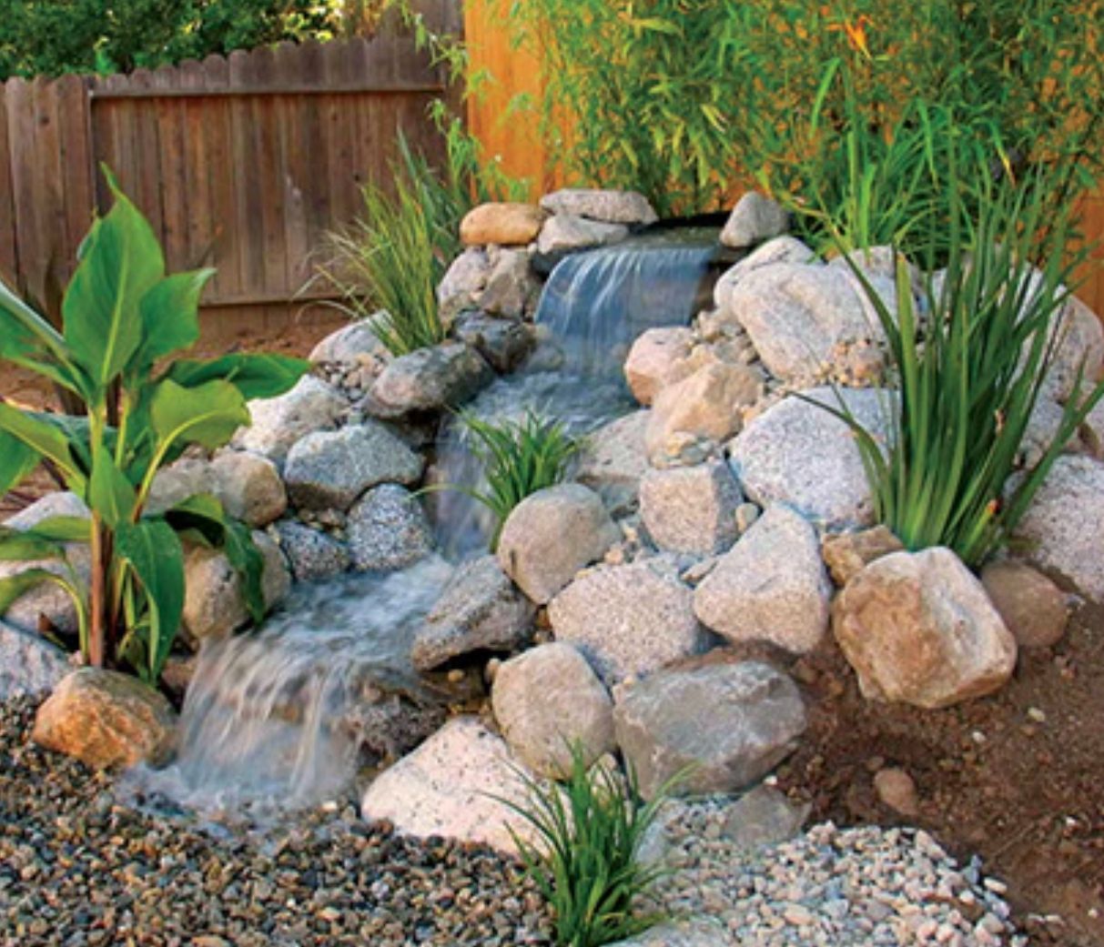Small backyard waterfall feature with rocks and greenery.