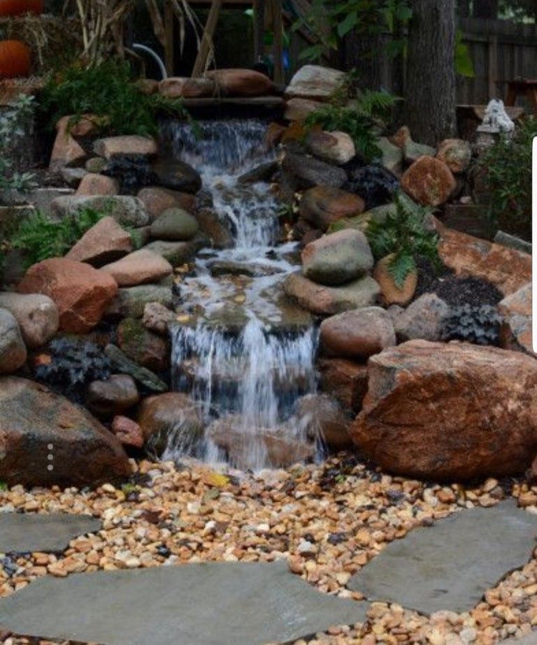 Small waterfall cascading over rocks in a garden, with stone path and gravel.