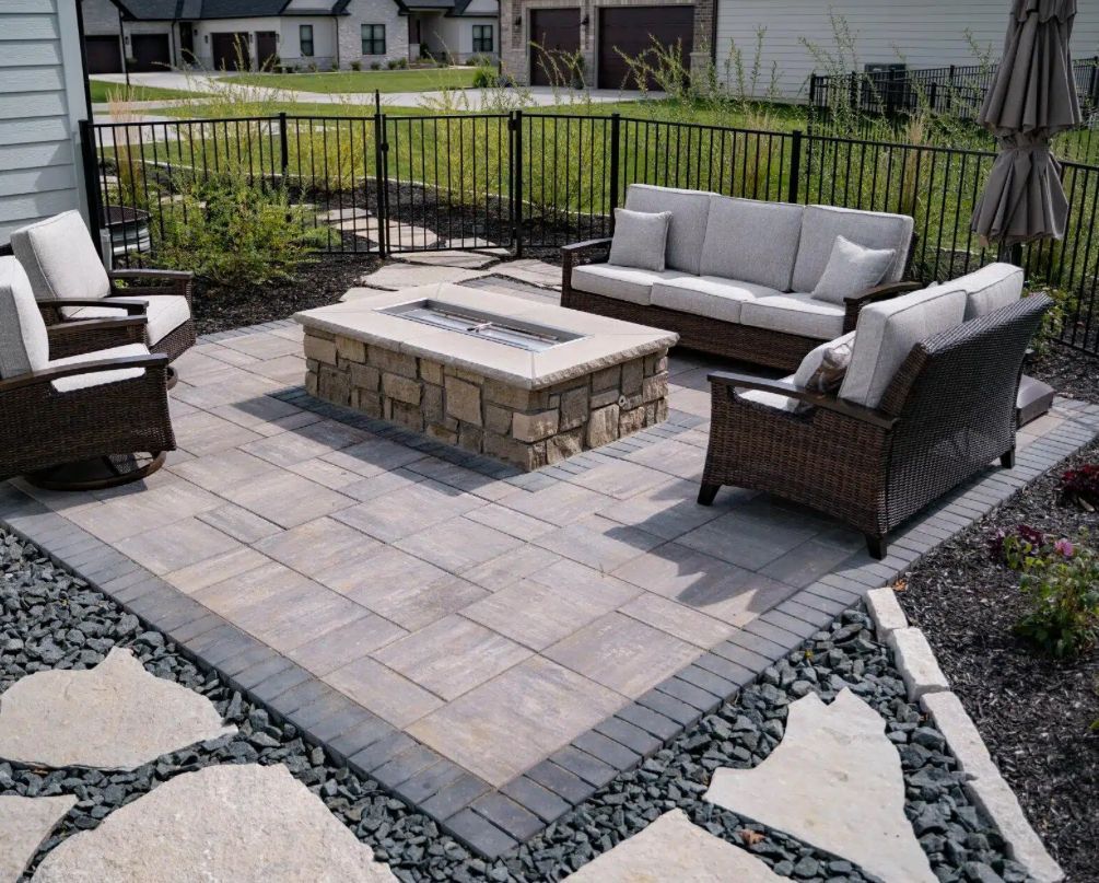 Patio with fire pit, seating, stone pavers, black fence, and decorative landscaping.