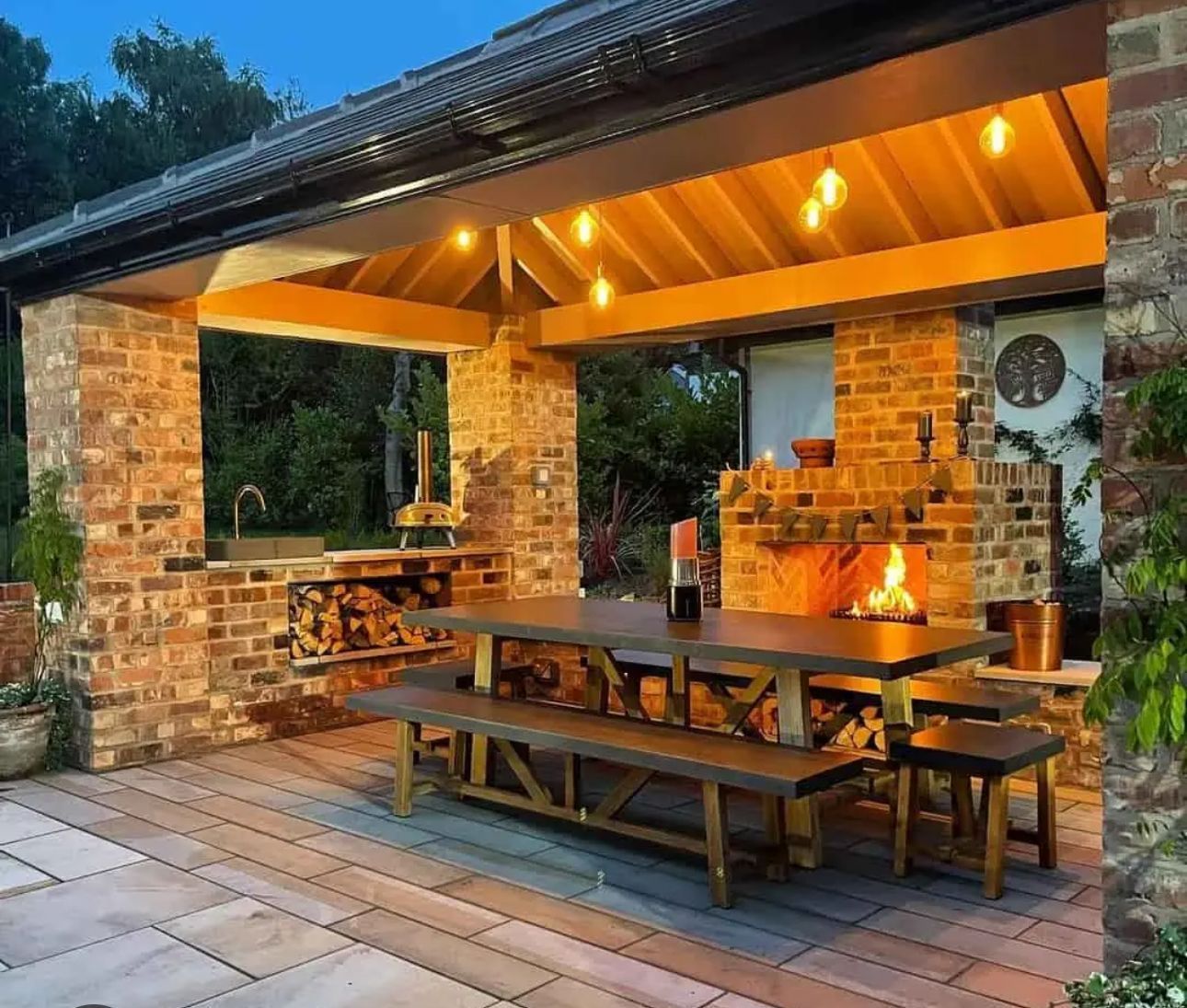 Outdoor brick patio with covered dining area, fireplace, and string lights at night.