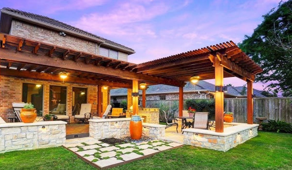 Backyard patio with wooden pergola, stone accents, outdoor lights, and lawn.