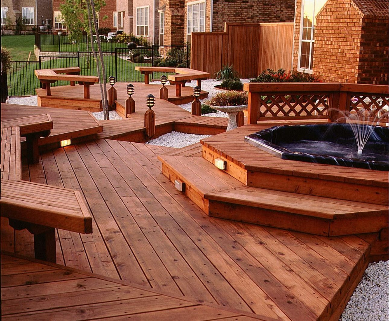 Wooden deck with a hot tub and built-in benches, set in a backyard.