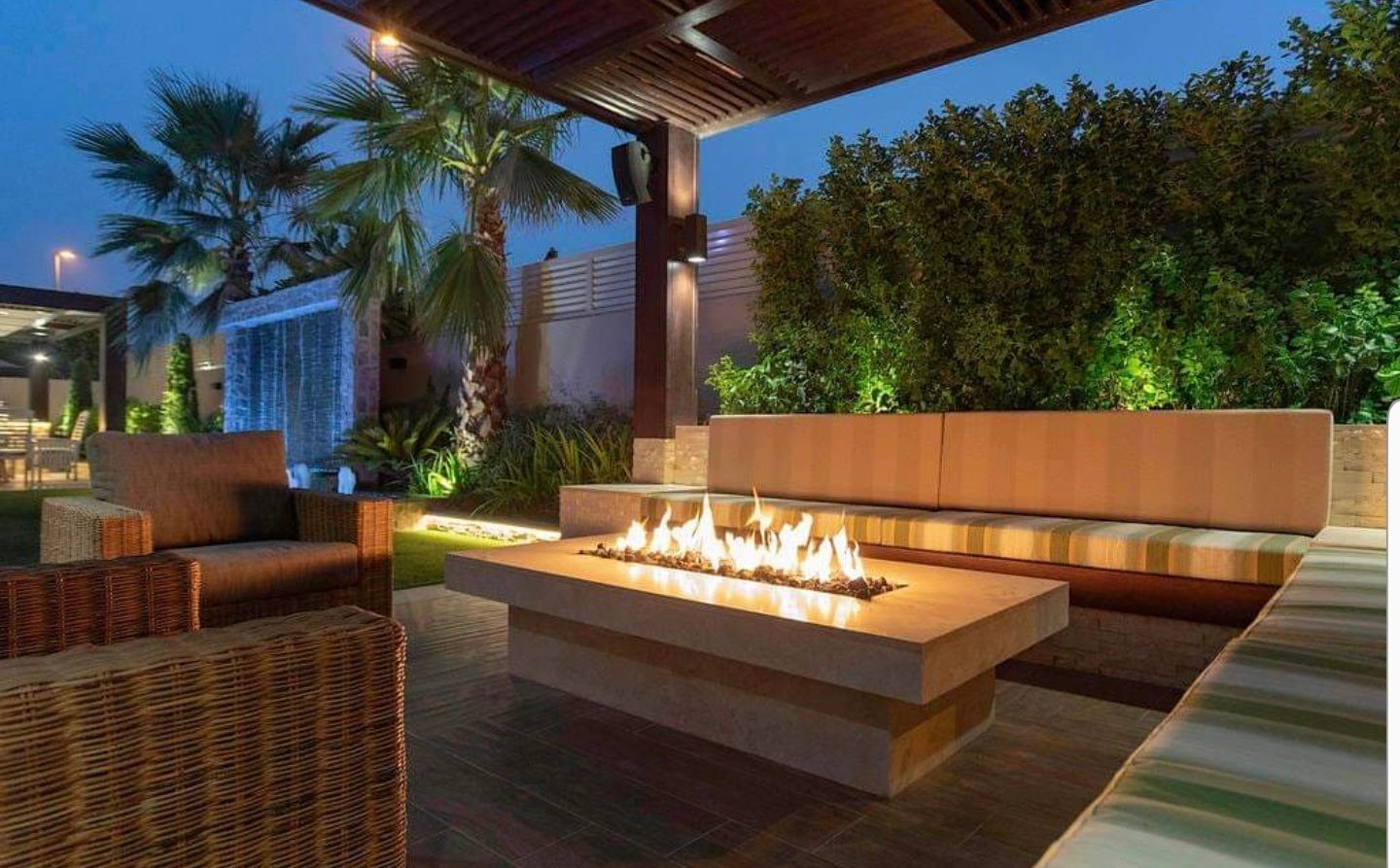 Outdoor seating area at dusk with fire pit, sofa, and waterfall.