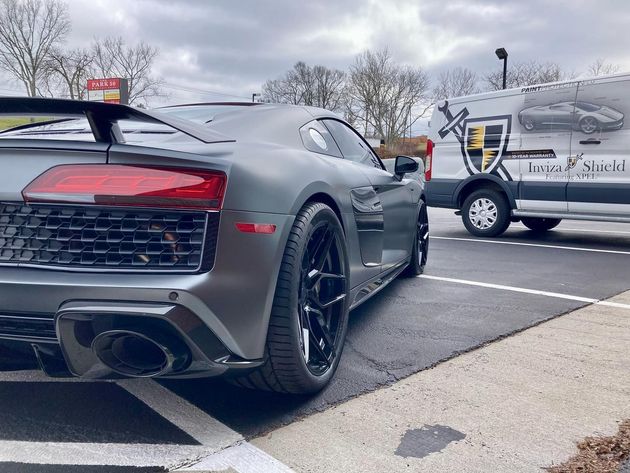 Dark gray sports car parked on a wet lot beside a white utility van with logo decals.