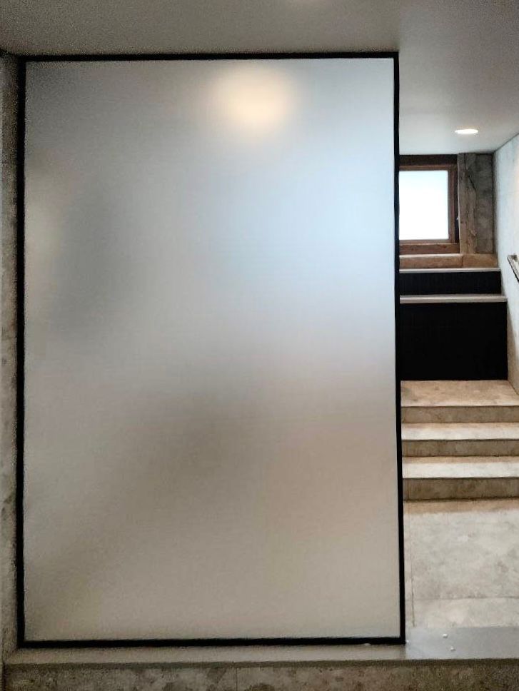 Frosted glass partition beside a carpeted stairway in a modern hallway with a small window.