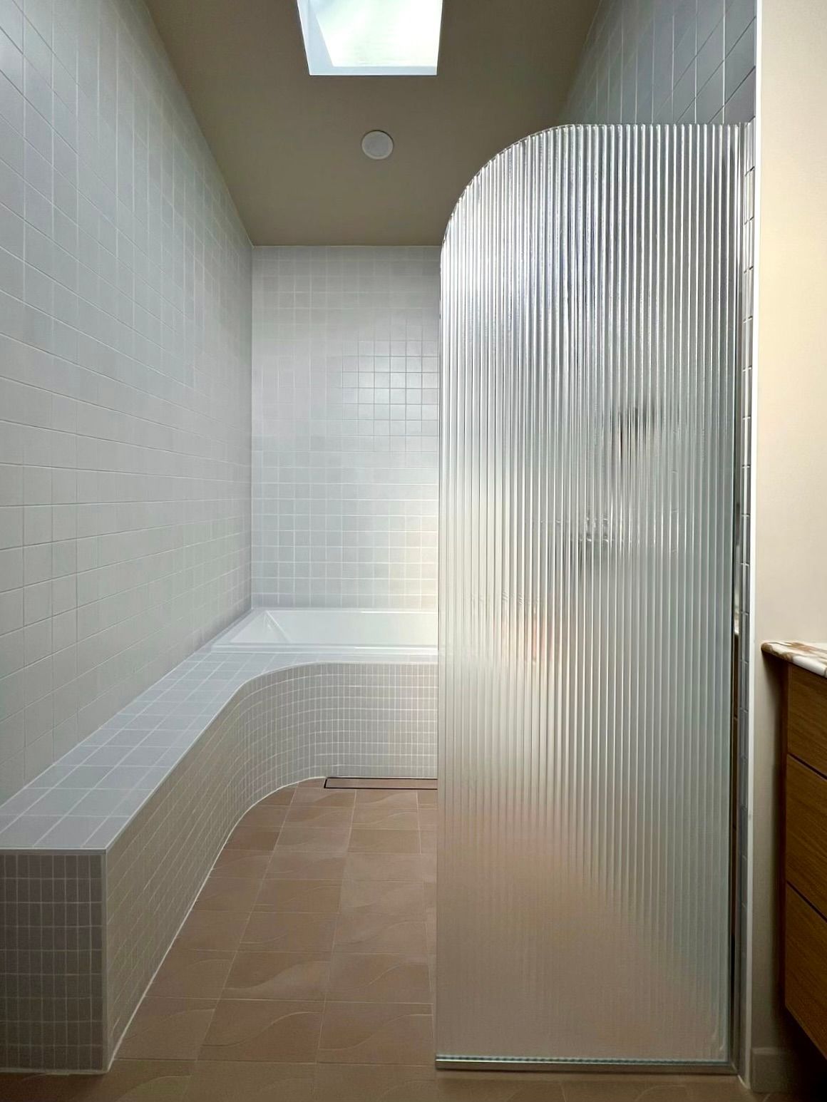 Small tiled shower room with a curved bench, white walls, tan floor, and frosted glass partition
