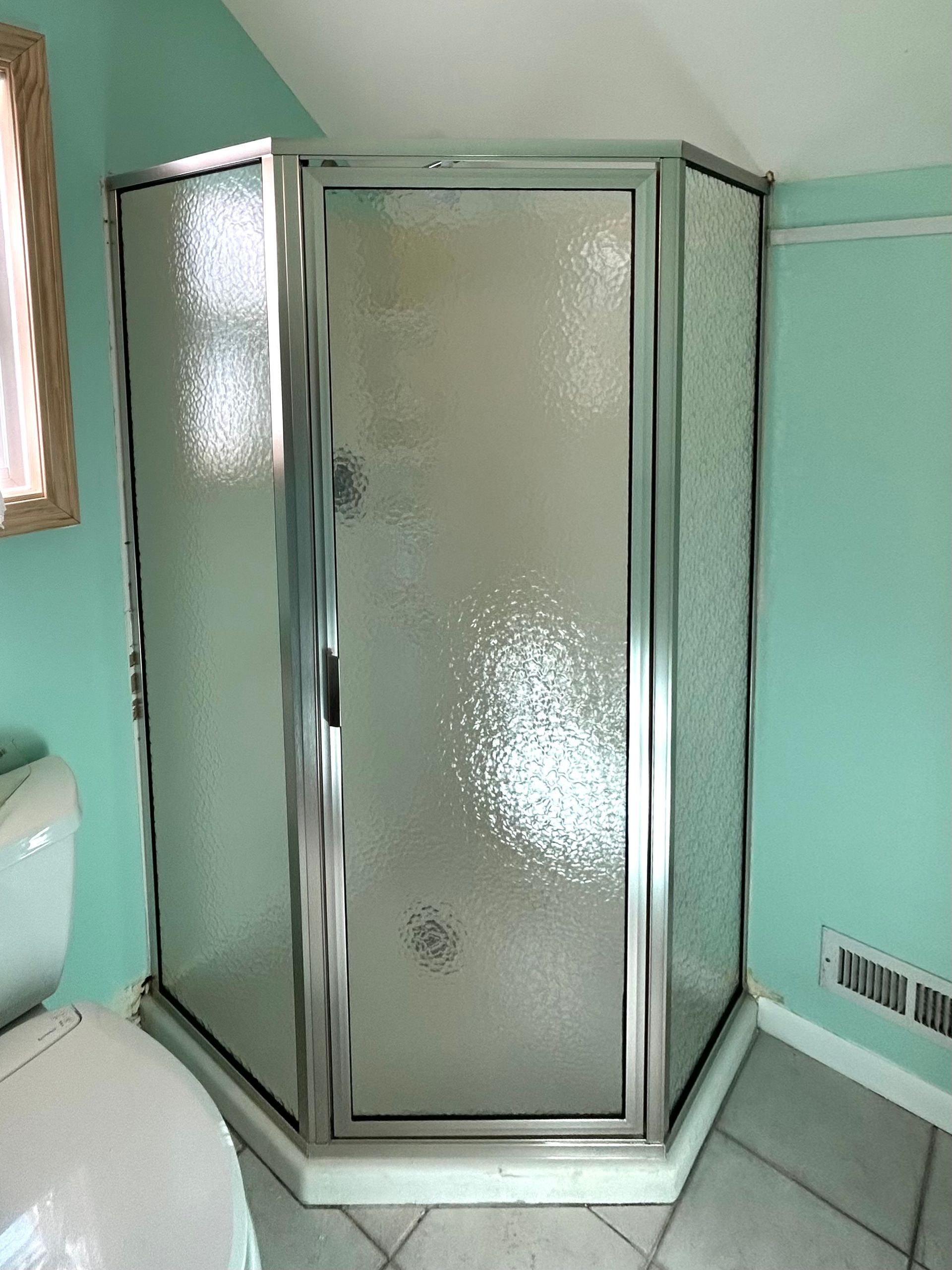 Frosted glass corner shower with chrome frame in a mint-green bathroom.