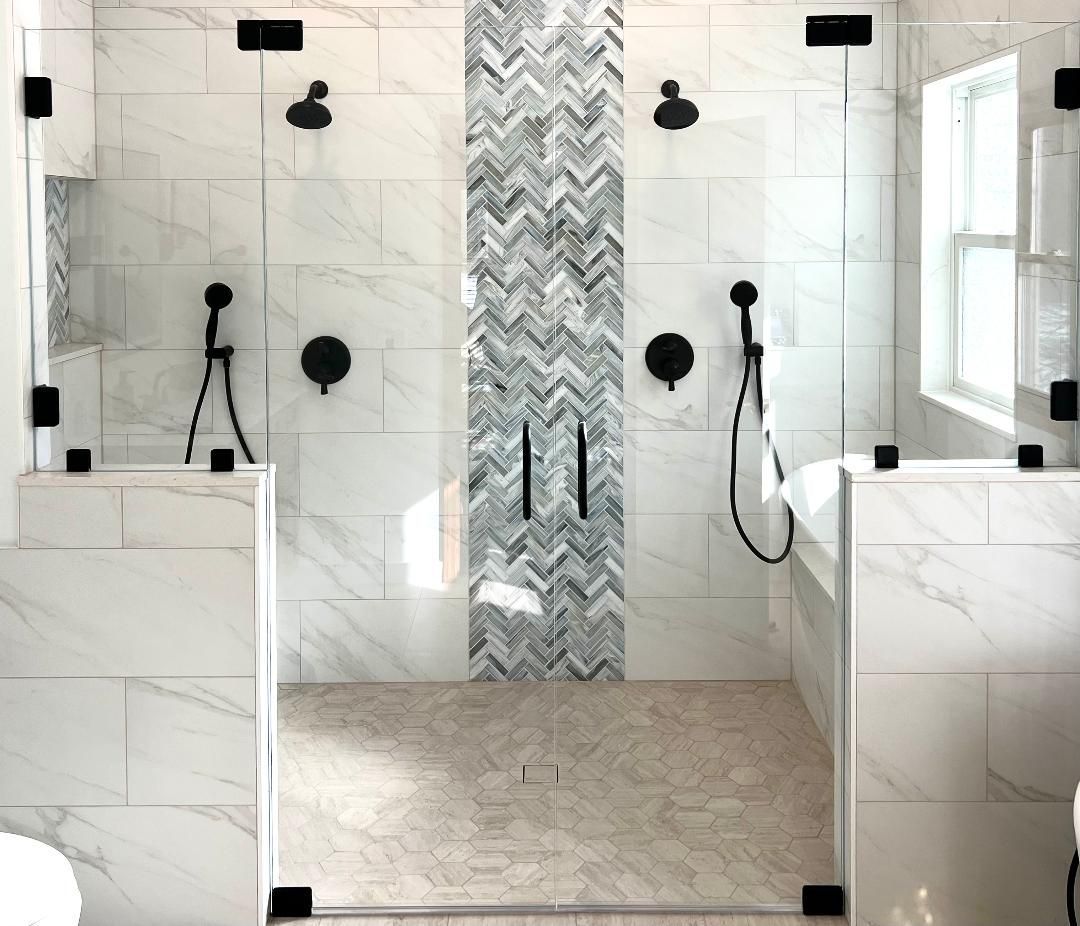 Modern bathroom shower with marble walls, chevron accent tile, black fixtures, and a built-in bench