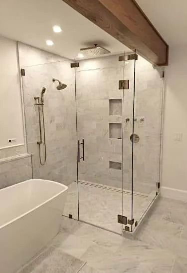 A modern bathroom featuring a white soaking tub next to a glass-enclosed shower with gray marble tile and a wooden beam.