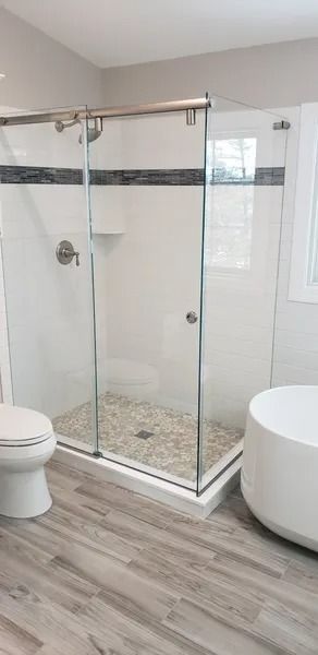 A modern bathroom featuring a glass shower stall with pebble flooring, a white toilet, and a freestanding bathtub.