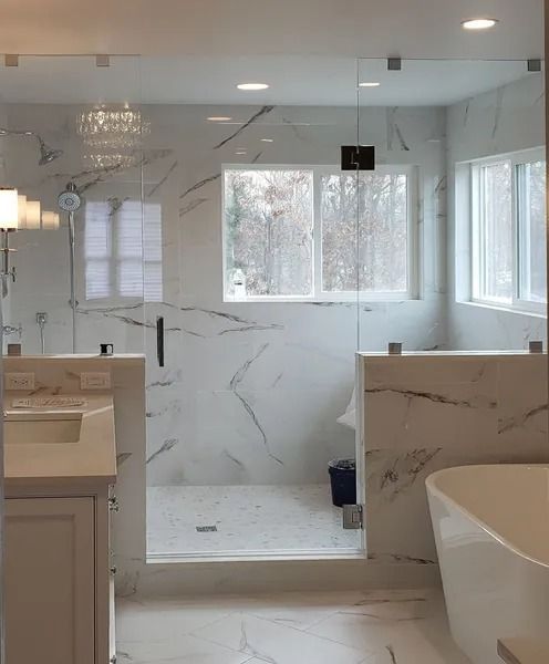 A modern bathroom features a glass-enclosed shower with white marble-patterned tile, a soaking tub, and a vanity.