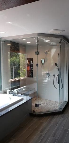 Modern bathroom featuring a corner glass walk-in shower with beige tile, a handheld showerhead, and a soaking tub.