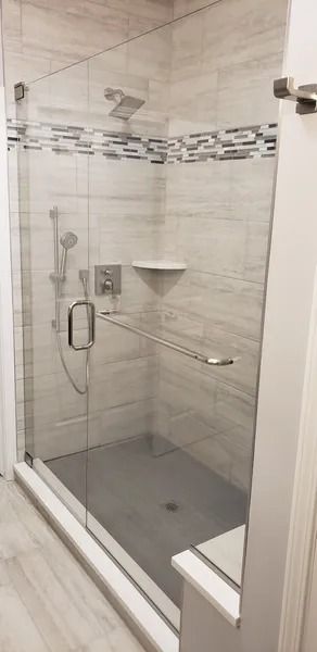 A walk-in shower with light-toned tiled walls, a grey base, a glass door, and silver shower fixtures.
