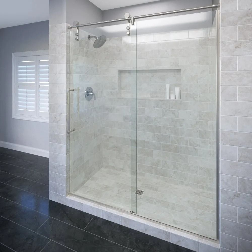 A modern glass shower enclosure with sliding doors, a stainless steel handle, and a recessed tiled wall niche.