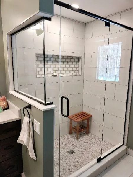 A glass-enclosed shower with white subway tiles, a mosaic-tiled niche, a wooden stool, and a black-framed sliding door.