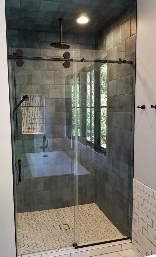 A walk-in shower with dark gray tiles, a rain shower head, glass sliding doors, and a small built-in soaking tub.