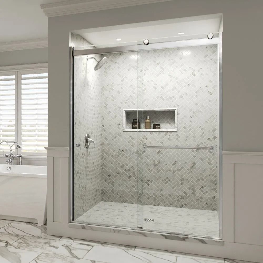 Modern walk-in shower with white herringbone marble tile, a built-in niche, and a sliding glass door in a neutral bathroom.