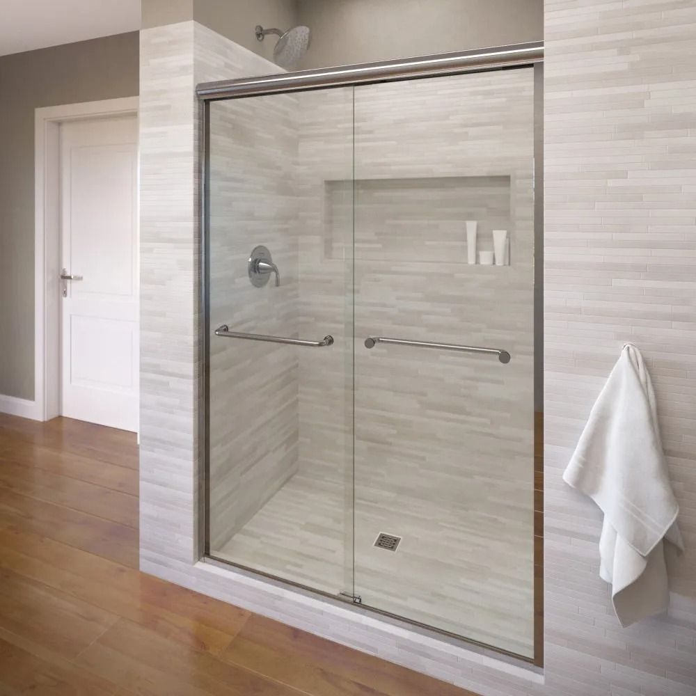 A modern walk-in shower with a sliding glass door, tiled walls, a built-in shelf, and a white towel hanging to the side.